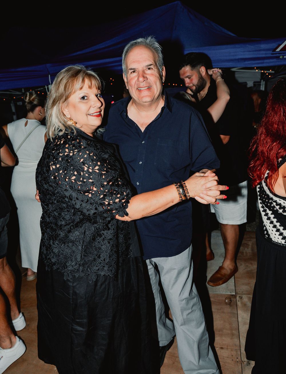 A couple dancing together at a nighttime outdoor event with other guests visible in the background.