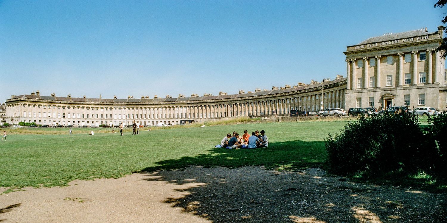 The iconic Royal Crescent in Bath, featuring Georgian architecture and a sweeping lawn under blue skies.