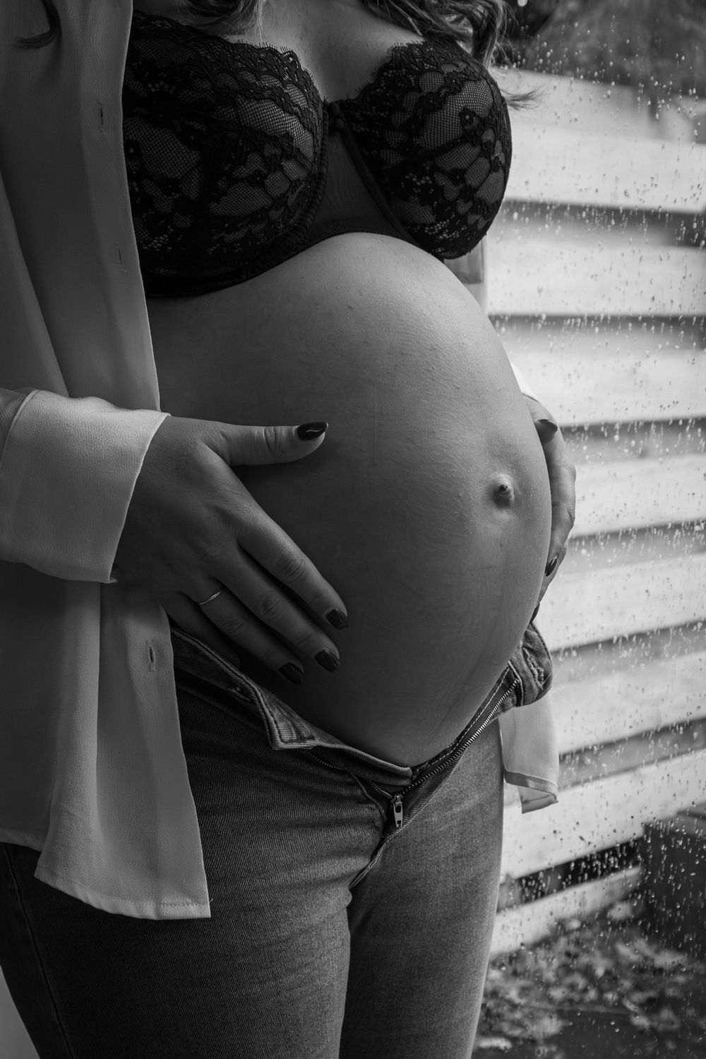 Black and white maternity photo showing pregnant belly against textured background.