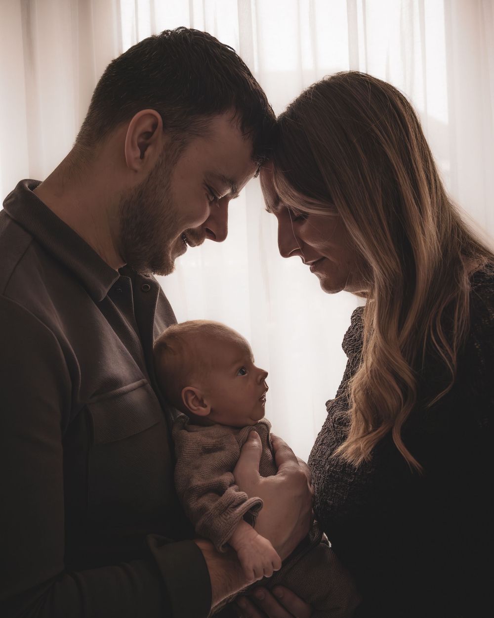 A couple shares an intimate moment with their baby in a series of five silhouetted photos by a window.