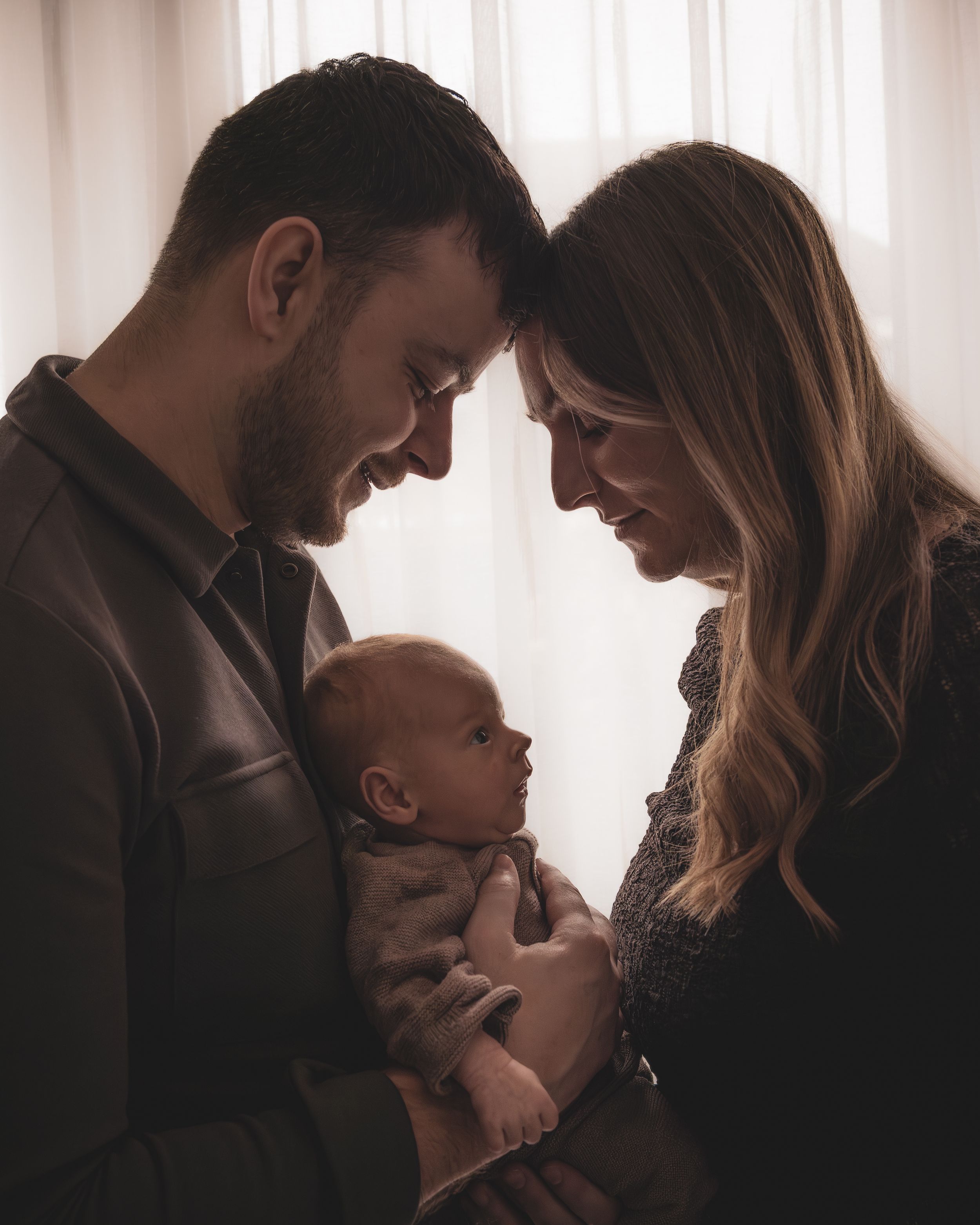 A couple shares an intimate moment with their baby in a series of five silhouetted photos by a window.