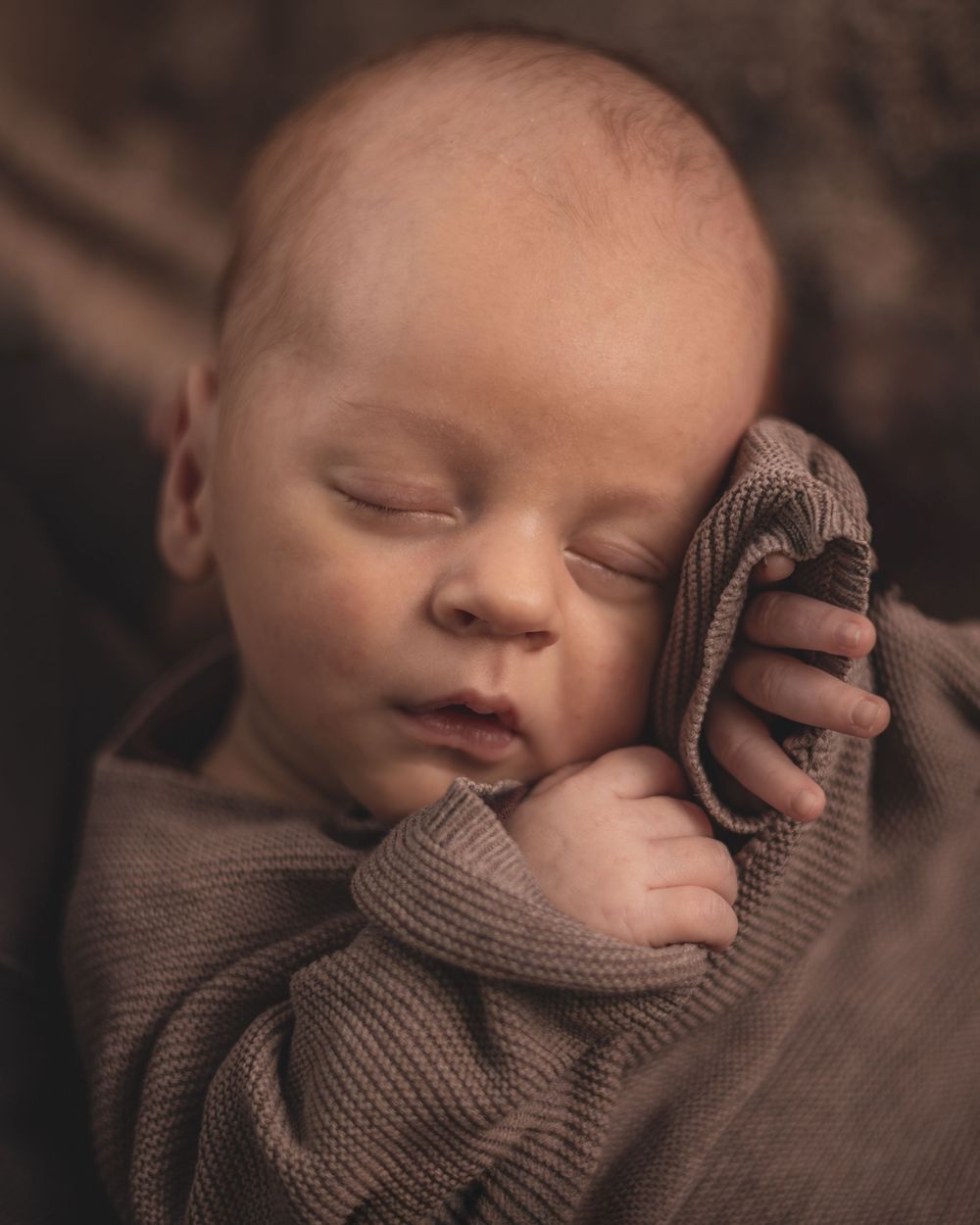 A sleeping newborn baby wrapped in a soft brown knit blanket is captured in a series of peaceful portraits.