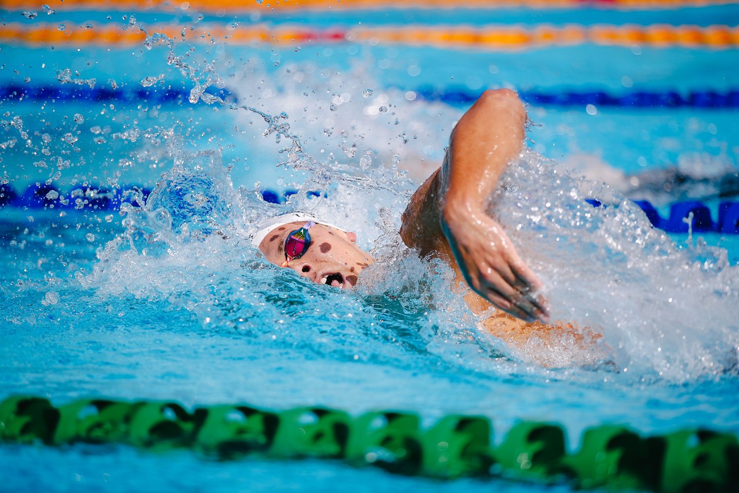 Competitive swimmer performs freestyle stroke creating dynamic water splash.