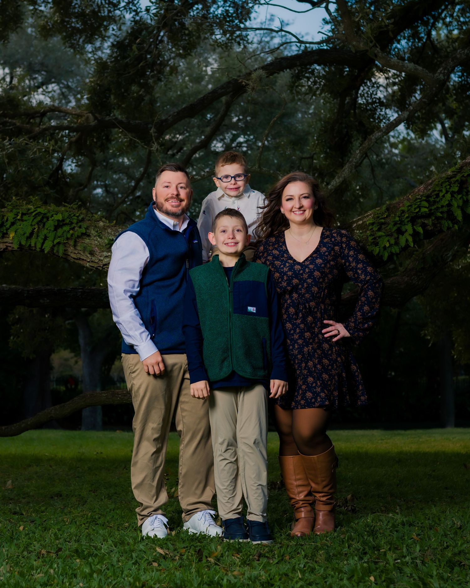 Family stands together in a garden with colorful flowers, wooden fence and trees in the background on a sunny day.