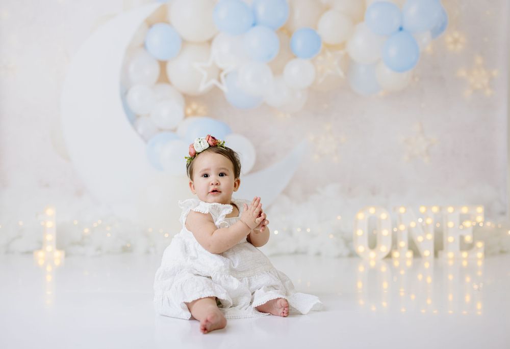 First birthday photo with soft blue and white balloon arch and twinkle lights.