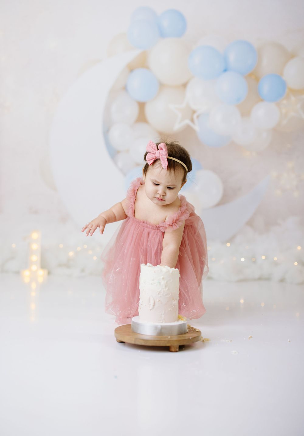 First birthday setup with moon prop, pink dress, and blue balloon arch.
