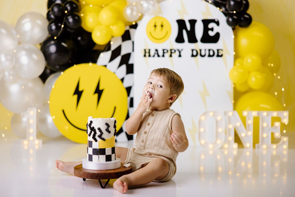 First birthday cake smash setup with yellow smiley face balloon decorations.