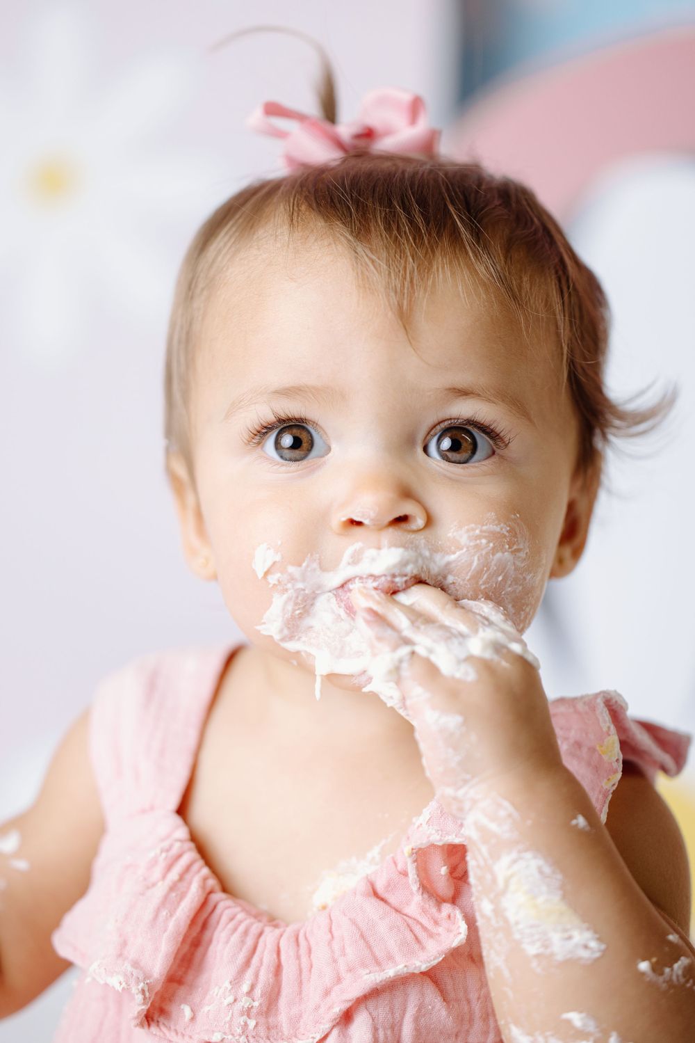 Baby in pink dress with cake frosting covered face during first birthday cake smash.