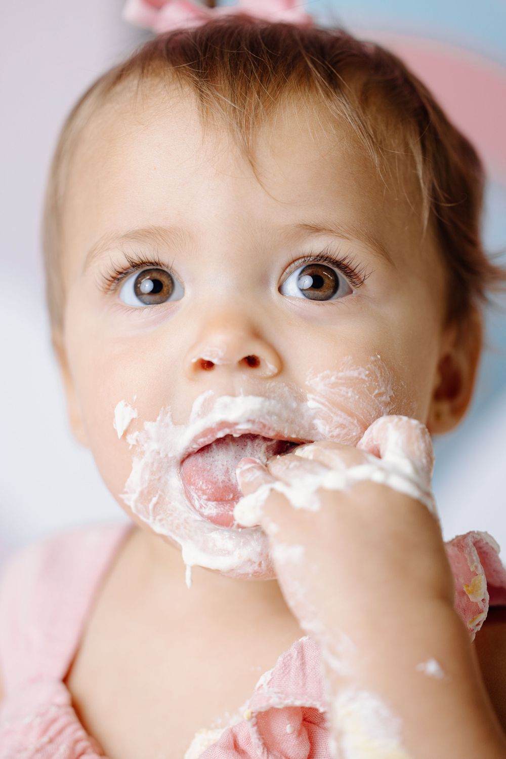 Close up of baby with messy cake frosting on face during birthday celebration.