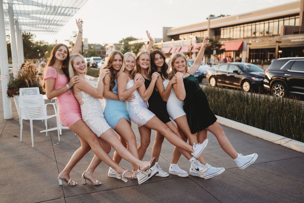 Friends in summer dresses striking a fun leaning pose together outdoors.