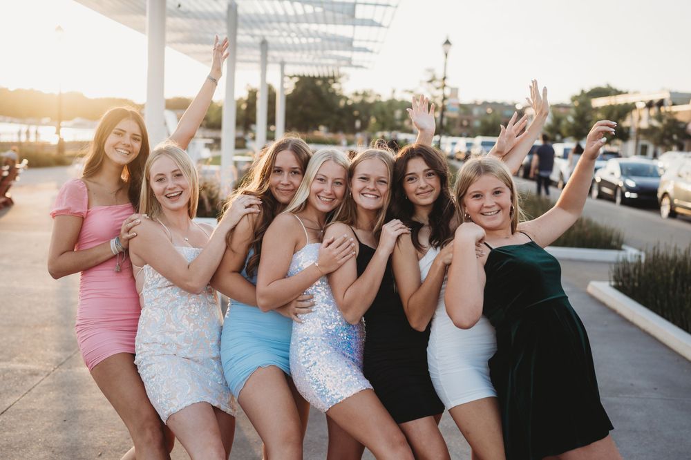 Group of friends in colorful dresses posing playfully at sunset.