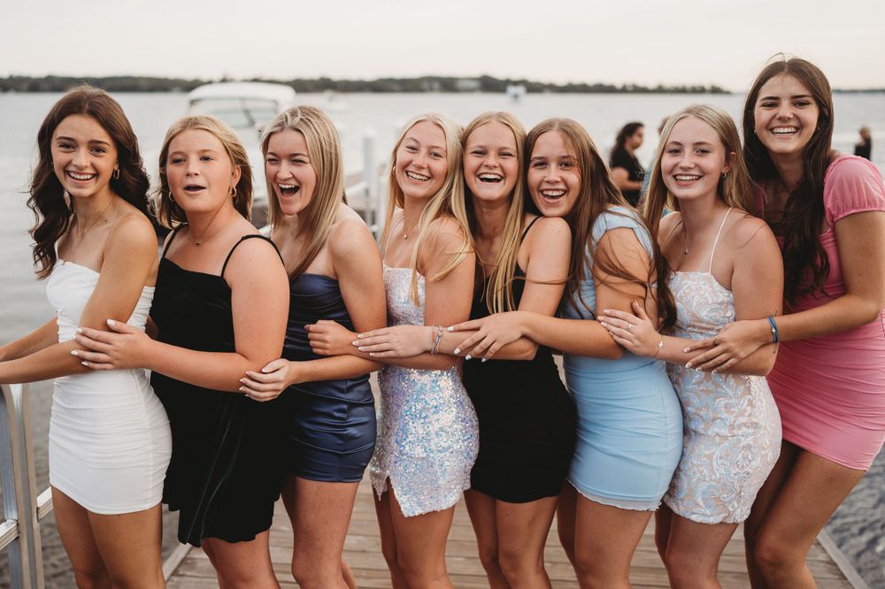 Row of friends standing together wearing coordinated summer outfits by the water.