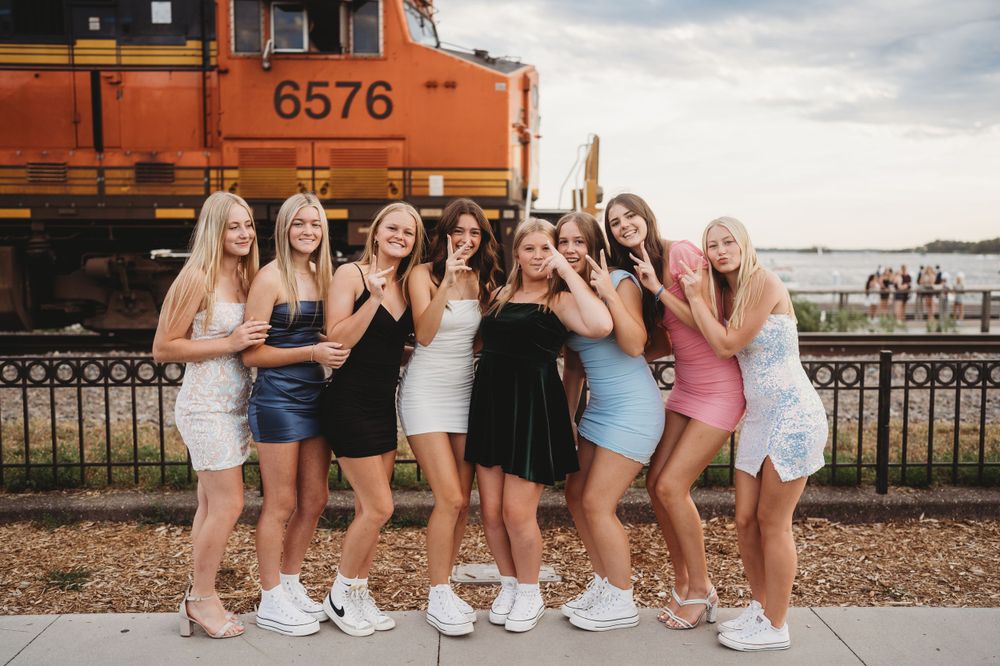 Friends posing together near train tracks and railings on a cloudy day.