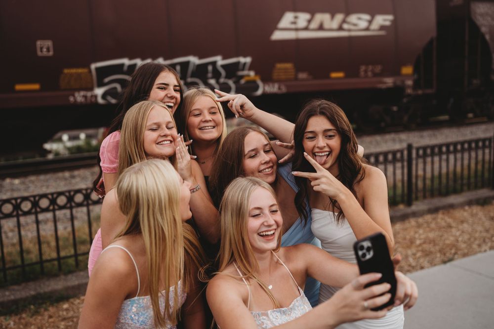 Group of friends taking selfies and making silly faces near a BNSF train car in the background.
