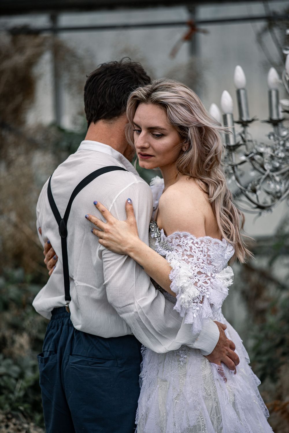 A couple in wedding attire embrace in a romantic dance pose with the bride wearing a white lace dress.