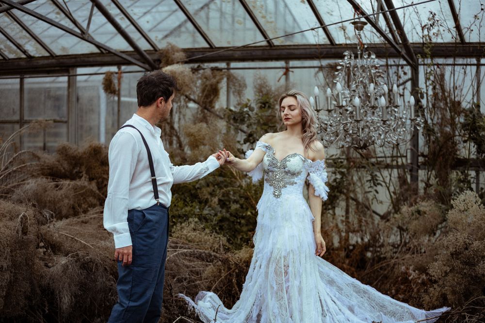 A romantic scene in a greenhouse with a vintage-style lace wedding dress and crystal chandelier overhead.