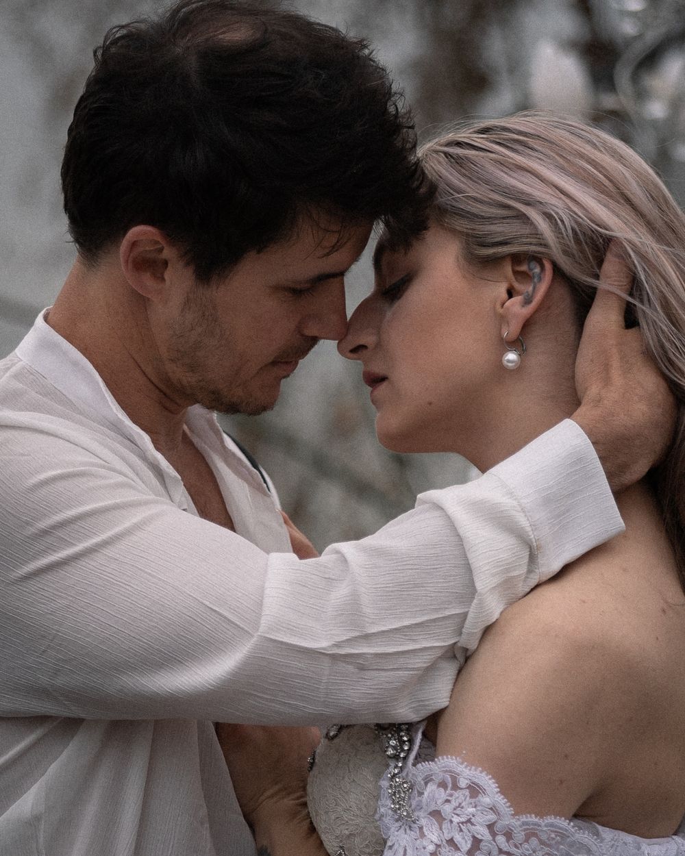 A romantic couple in white attire share an intimate moment during a wedding photoshoot.