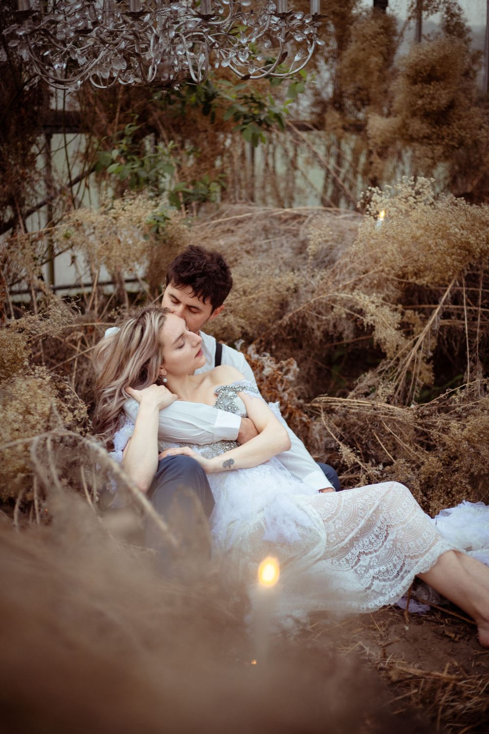 A romantic couple in white attire reclines together on a rustic outdoor setting during a dreamy photoshoot.