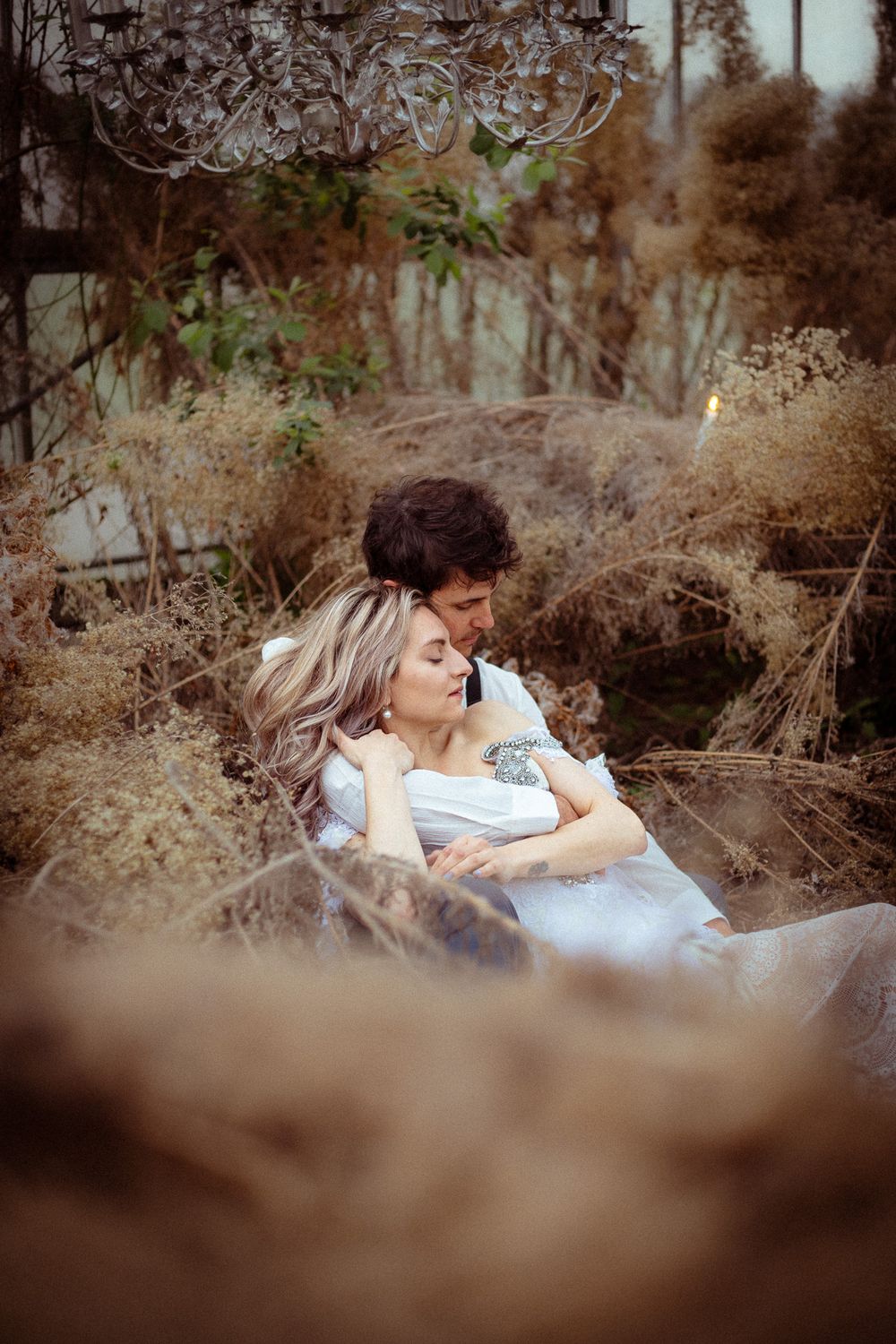 A romantic couple shares an intimate moment lying together in a rustic outdoor setting with soft natural lighting.