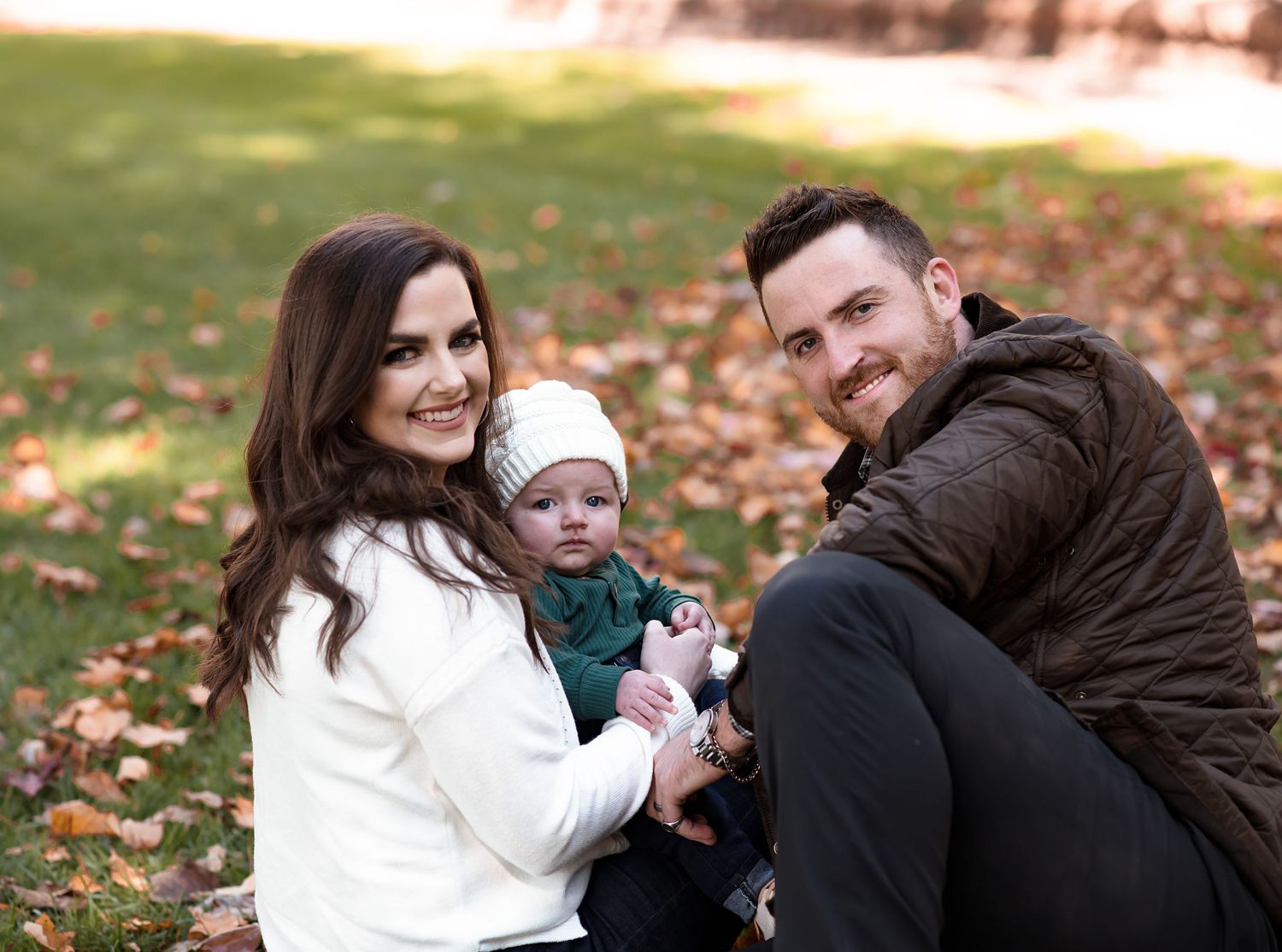 Family sitting together on fallen autumn leaves in casual outdoor setting.