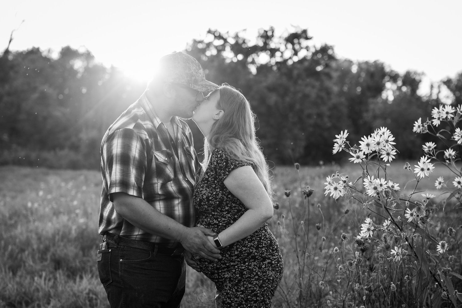Black and white portrait of a couple embracing in a wildflower meadow at sunset.
