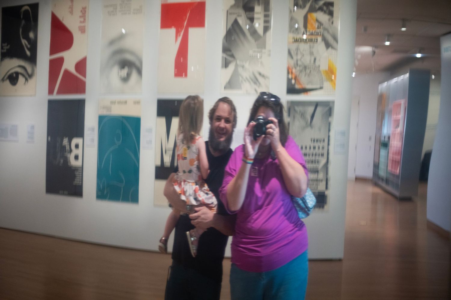 Two people posing in an art gallery with colorful graphic design posters displayed on the wall behind them.