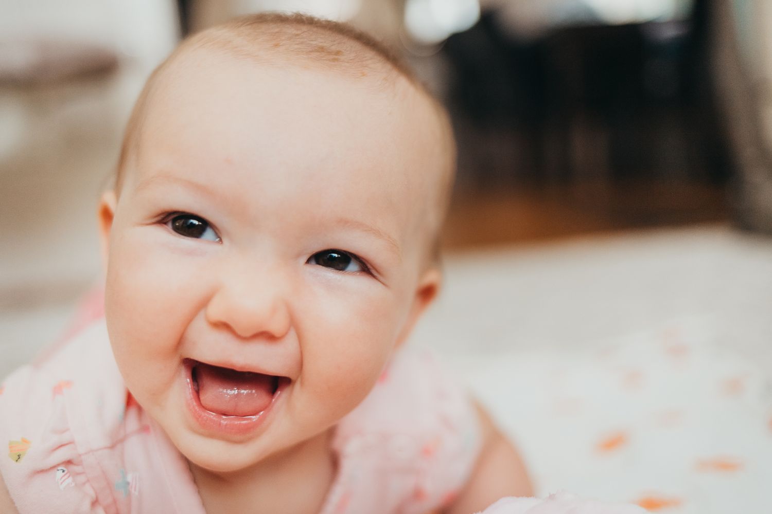 Smiling young girl lying next to a happy baby on a soft blanket, siblings sharing a joyful moment together.