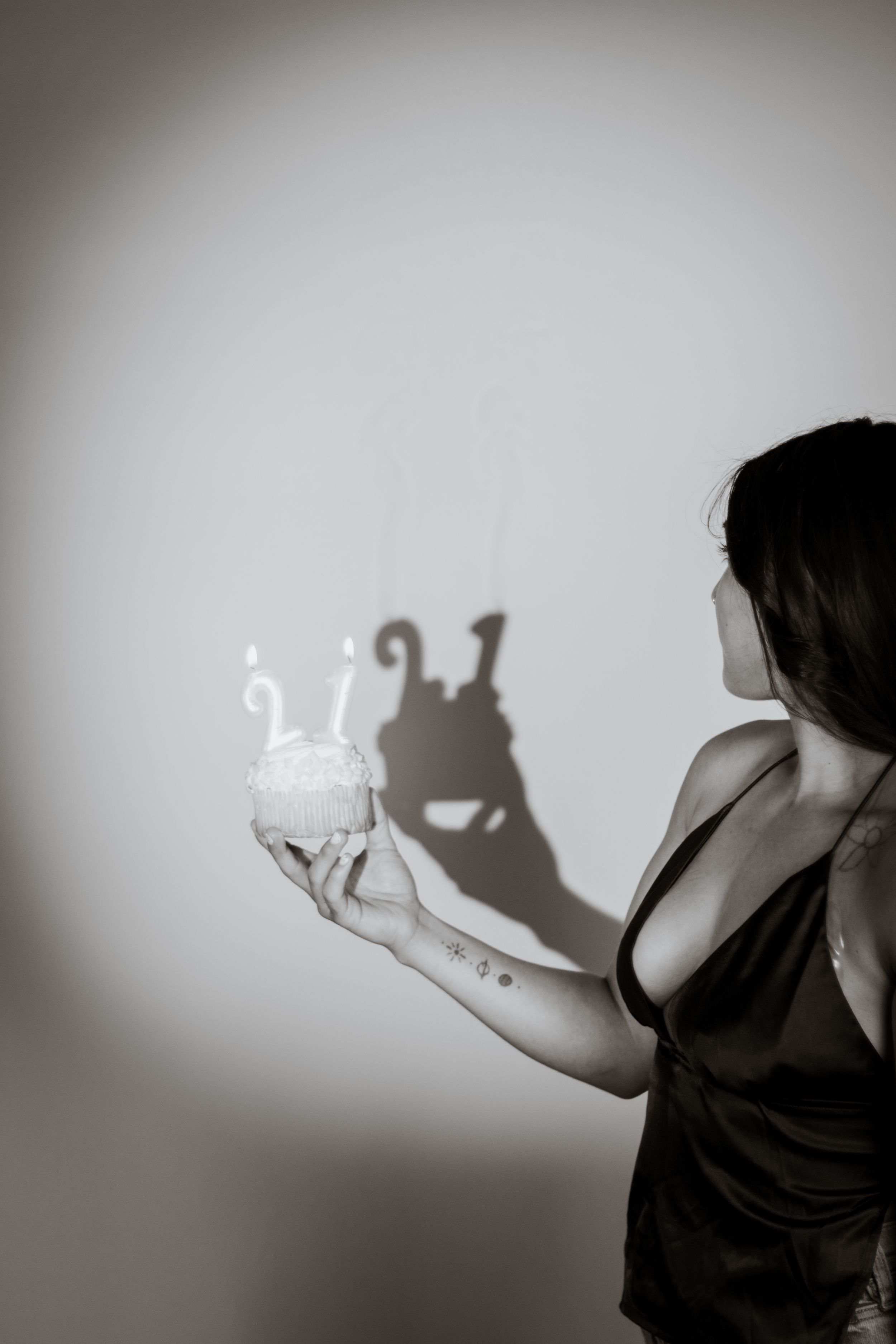 Black and white photo of woman holding small birthday cake with lit candles against wall taken by a pierce county photographer in studio