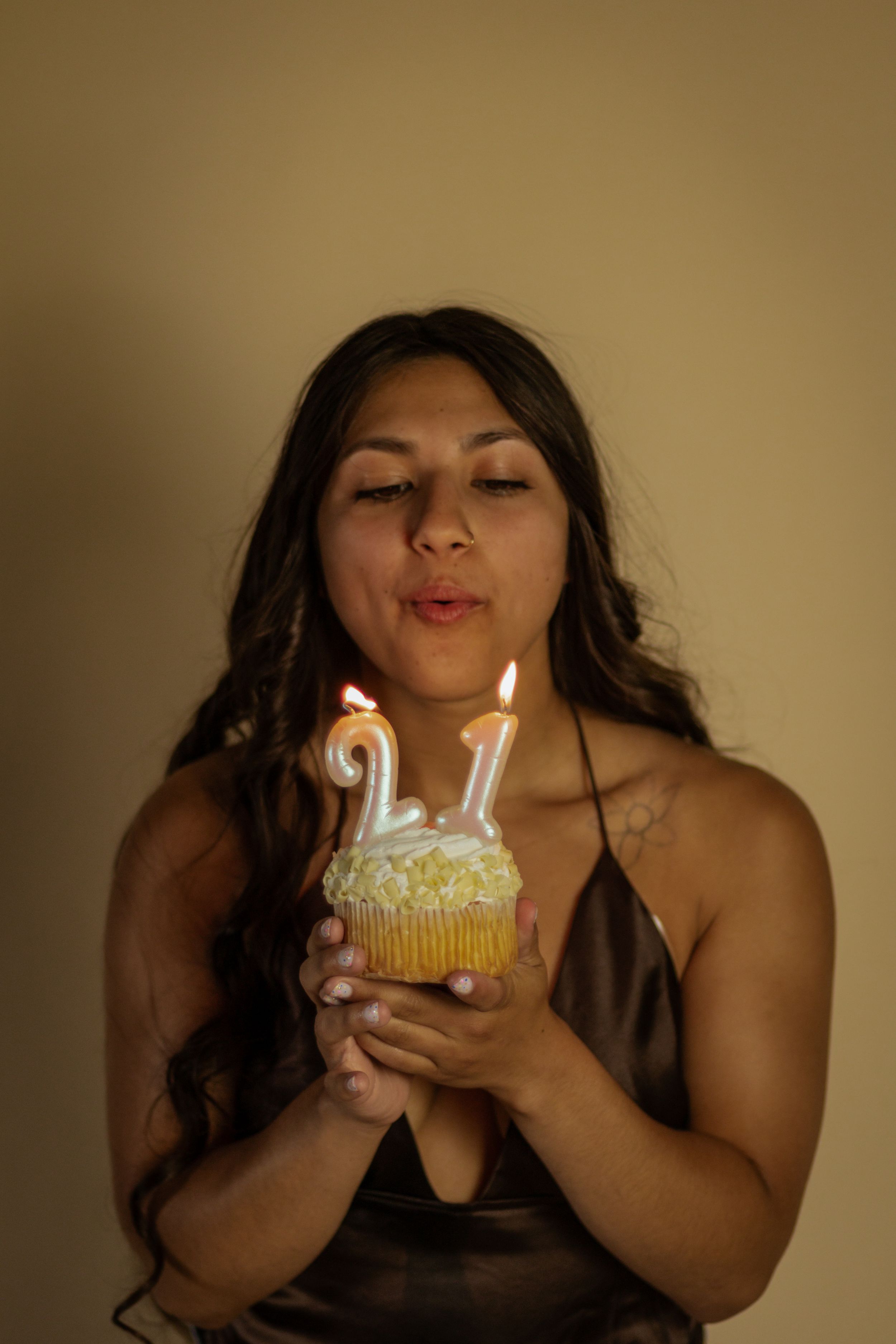Young woman blowing out number 21 candles on a birthday cupcake, celebrating her 21st birthday photographed by roy wa photographer