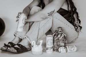 Black and white photo of woman sitting with sandals, cans, and decorative items on floor of pierce county mini photography studio
