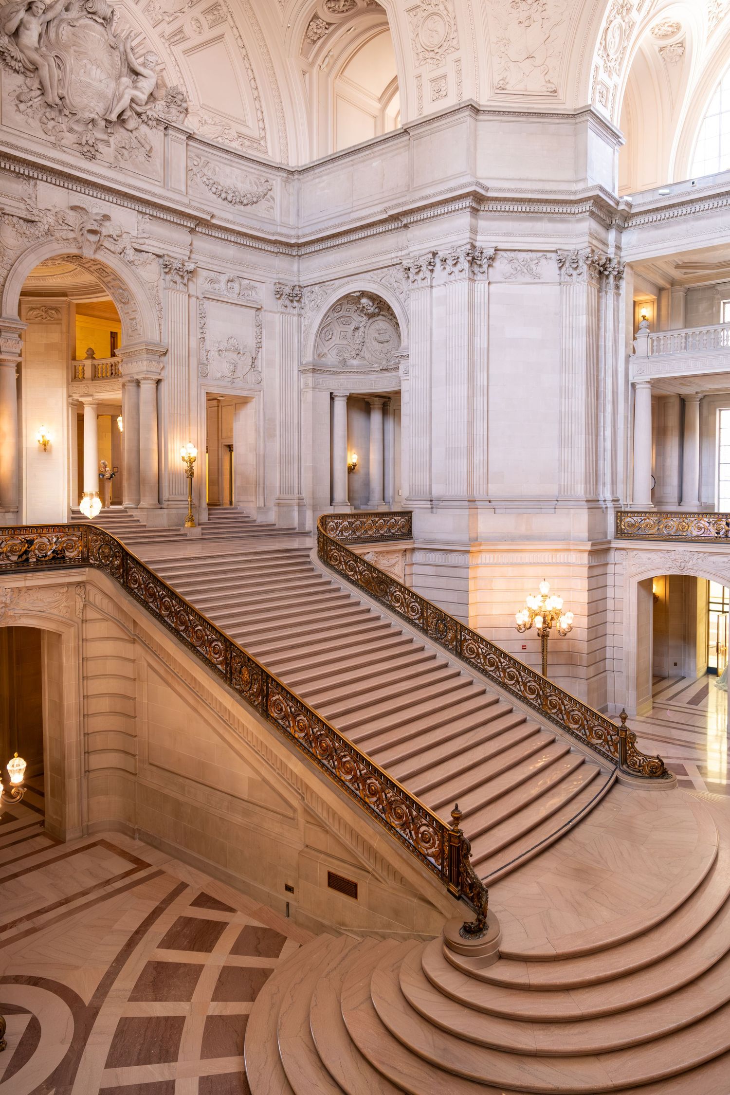 Grand marble staircase with ornate iron railings inside San Francisco City Hall's Beaux-Arts rotunda.