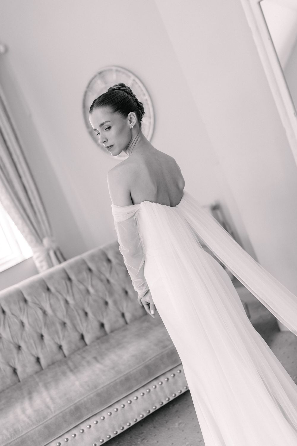 Elegant bride in a backless white gown with flowing skirt poses gracefully in a luxurious room.