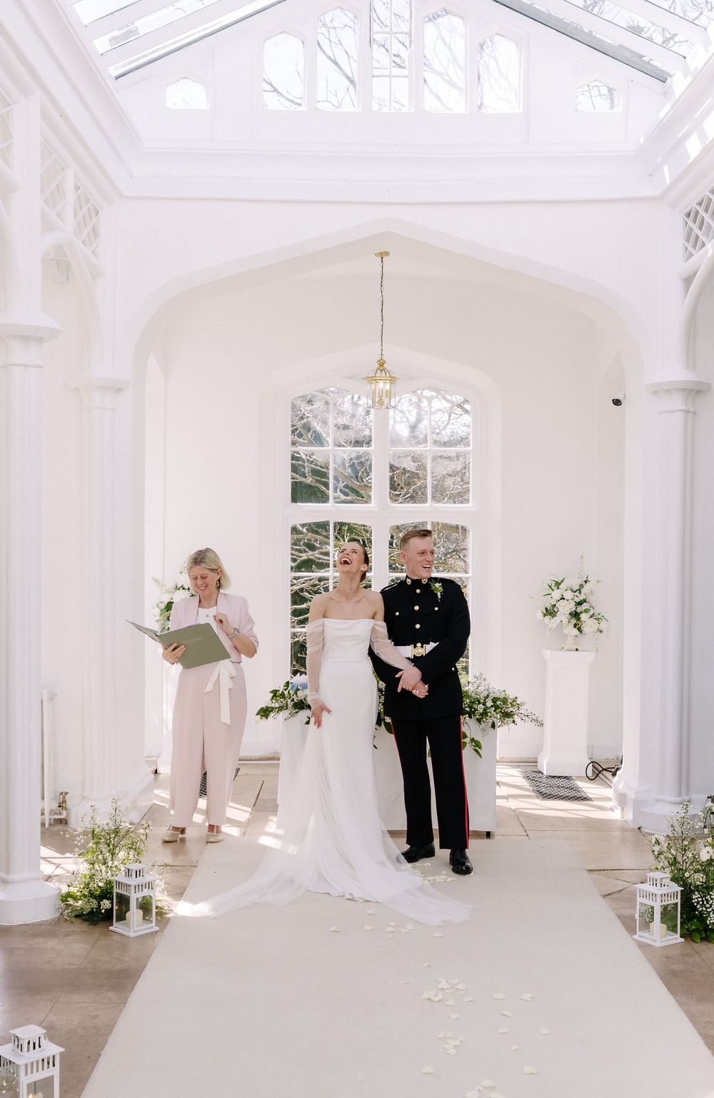 Bride and groom stand at the altar in an elegant white conservatory chapel during their wedding ceremony.