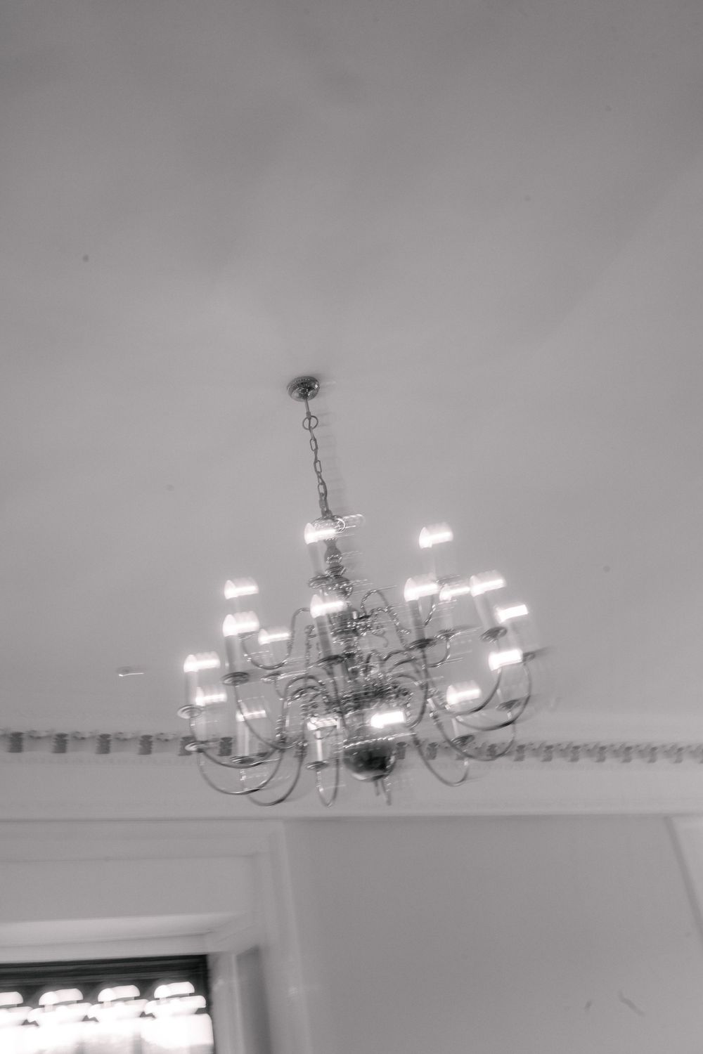 Ornate multi-arm chandelier with glowing bulbs hanging from a white ceiling in an elegant room.