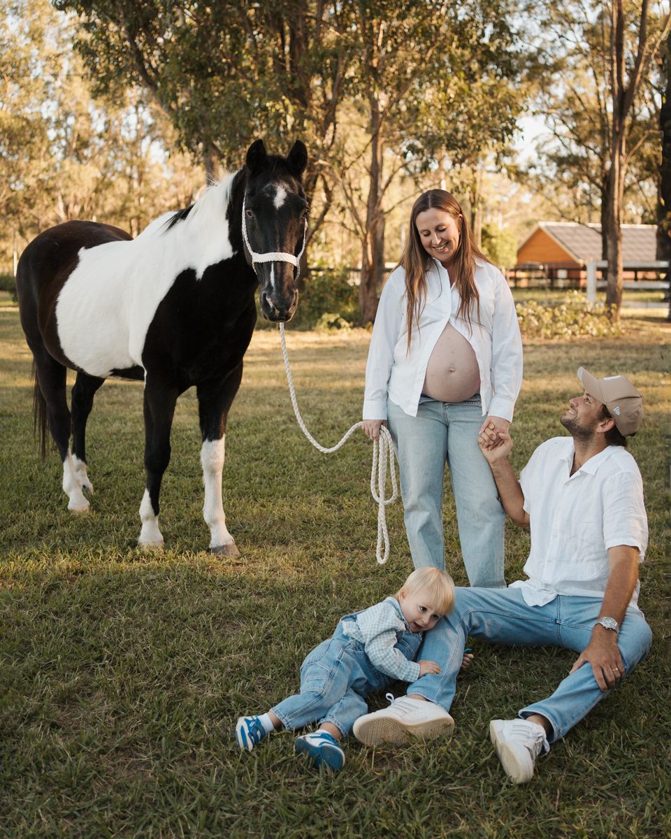 Pregnant woman with partner and toddler posing beside a black and white horse on a sunny farm during a photoshoot in sydney