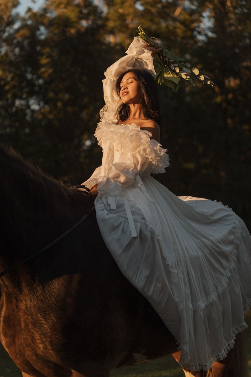 Woman in white dress and floral hat rides horse at golden hour sunset during a romantic couples photoshoot in sydney