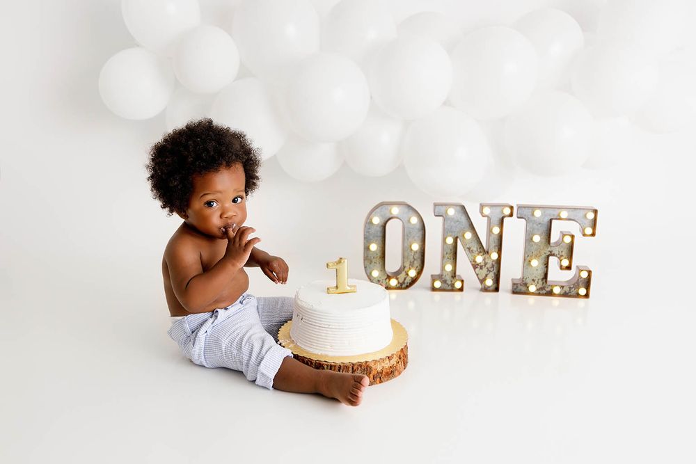 Baby's first birthday cake smash photo with ONE marquee letters and white balloons backdrop by Moreno Valley baby photographer.
