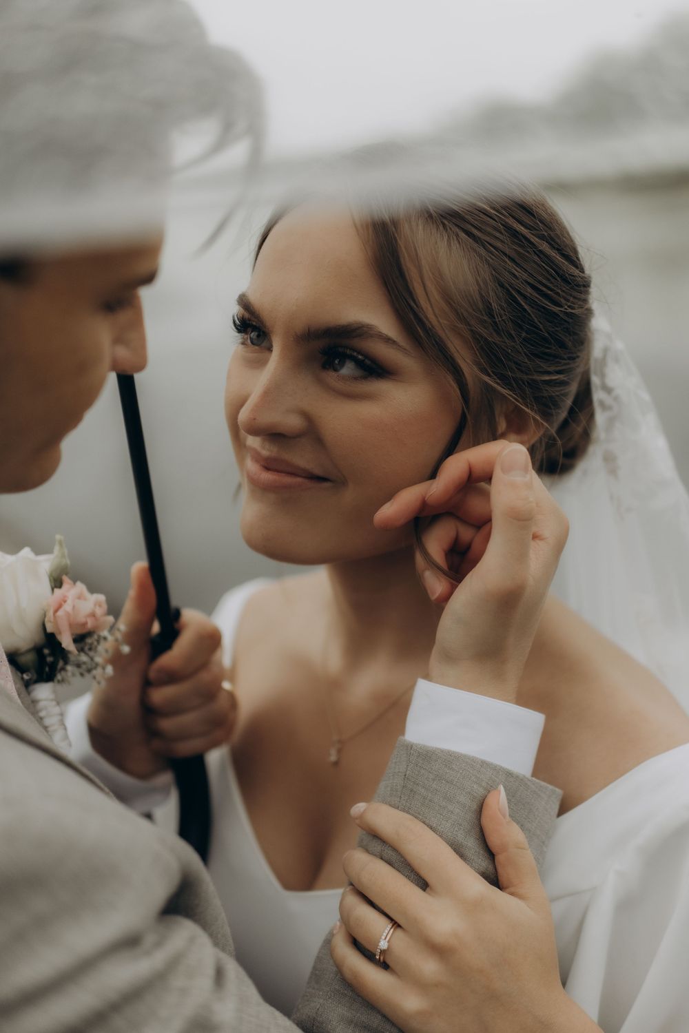 groom stroking bride's face standing under an umbrella in rain while being captured by documentary relaxed wedding photographer in Stockholm