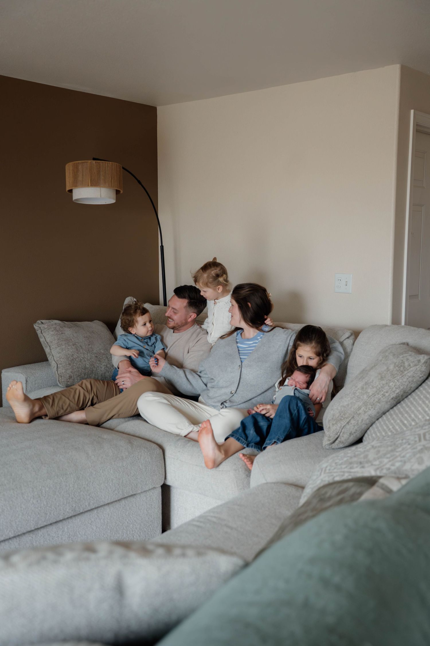 A joyful mother lifts her laughing toddler overhead while sitting cross-legged on a bed in a cozy bedroom.