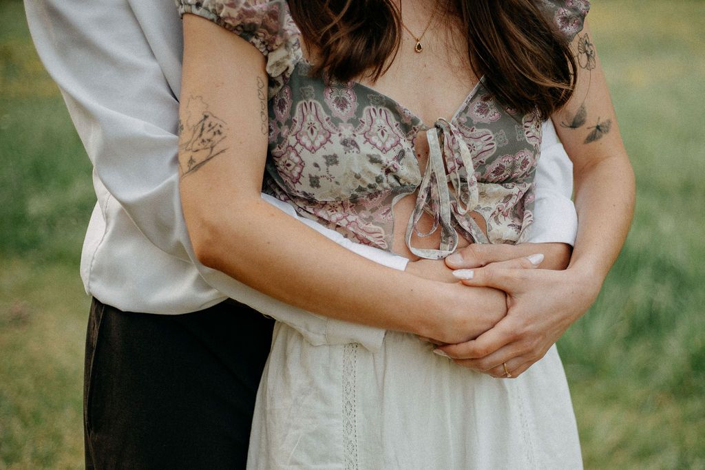 Close-up of a couple embracing, showcasing the woman's floral tattoo and delicate ring detail.