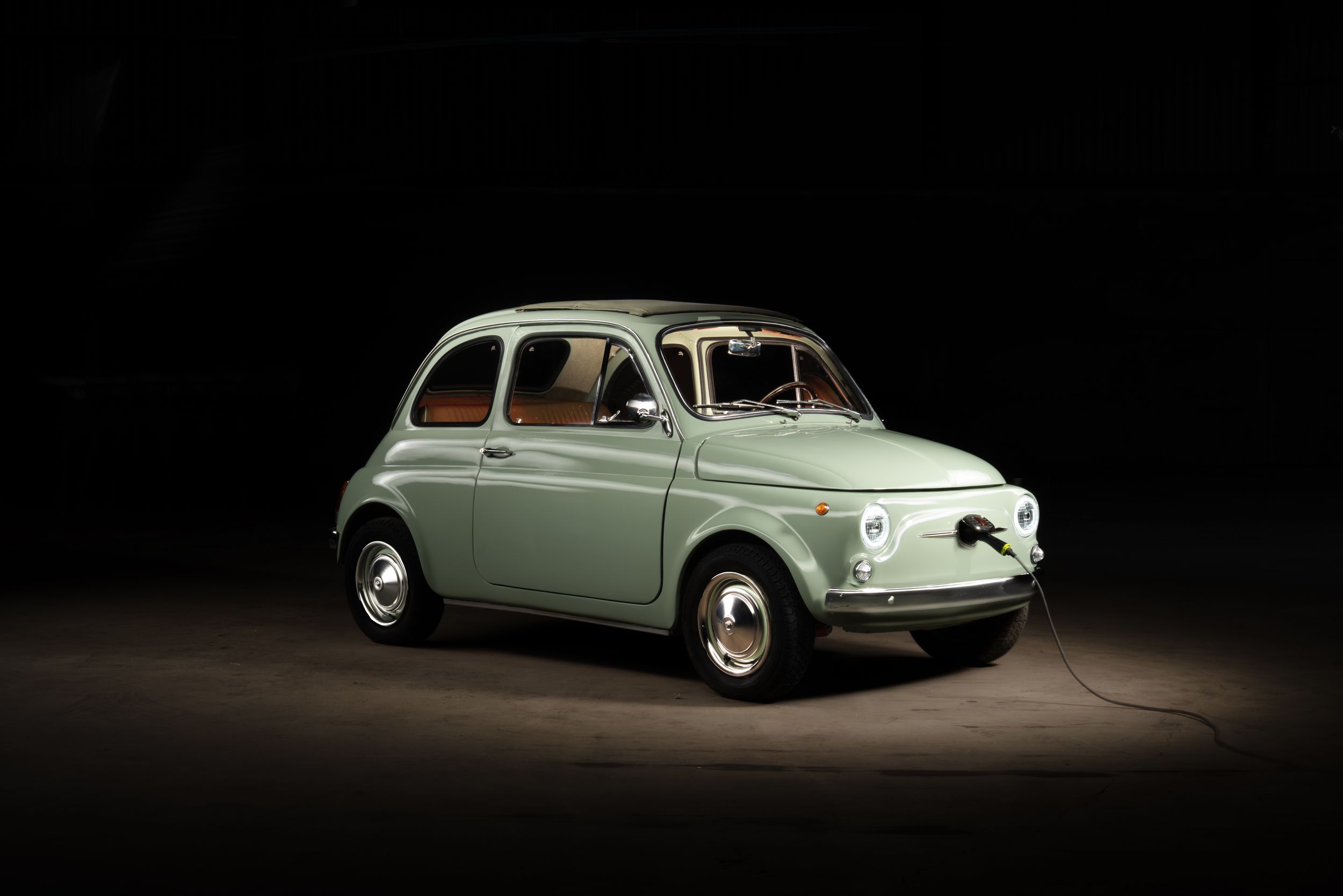 Vintage mint green Fiat 500 classic car displayed in dramatic studio spotlight against dark background.