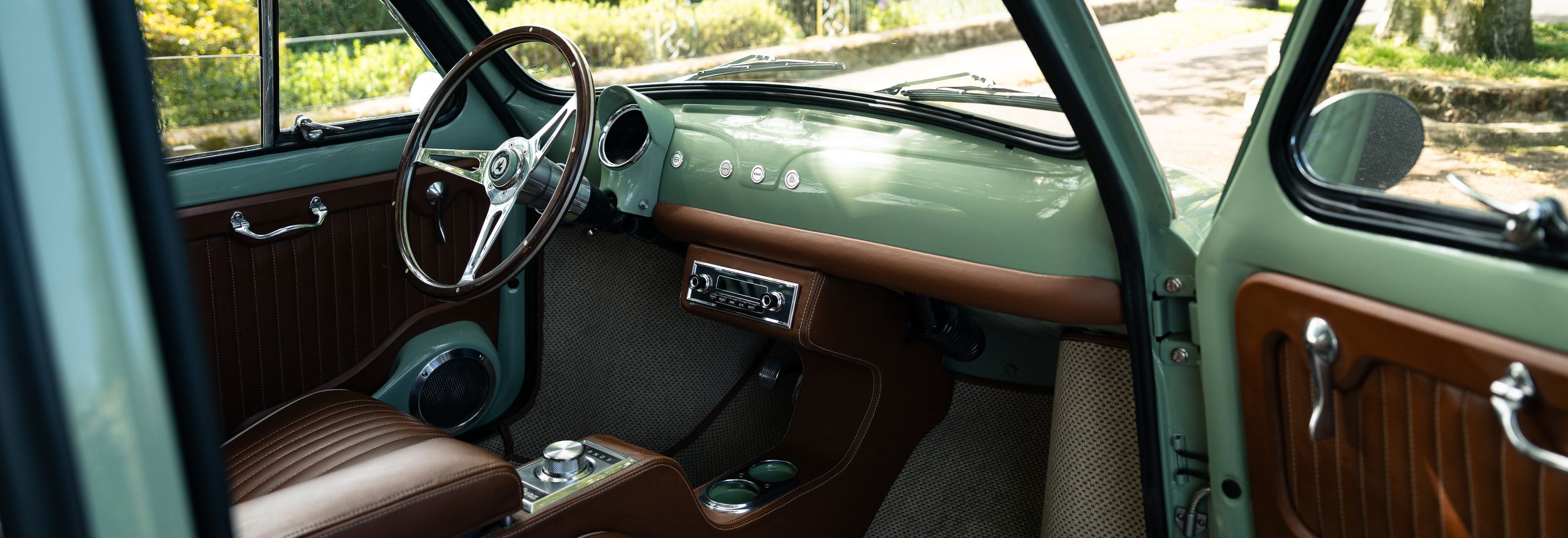 Vintage car interior with green dashboard, wood trim, brown leather seats, and classic steering wheel.