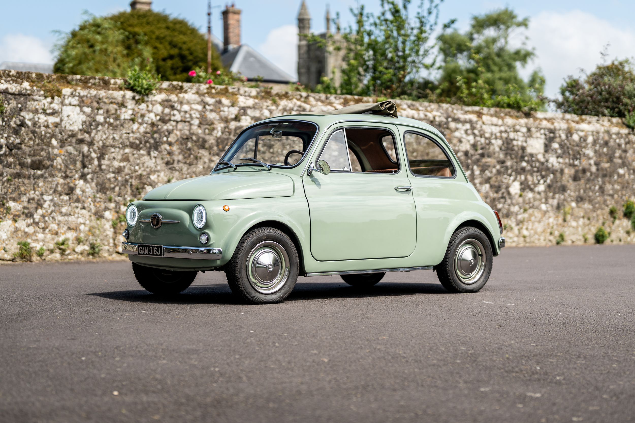 Classic mint green Fiat 500 vintage car parked on pavement beside a stone wall.