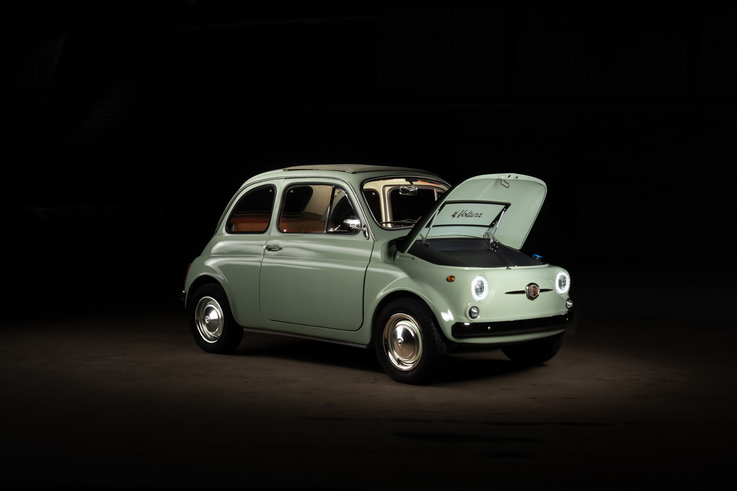 Classic mint green Fiat 500 vintage car with open hood displayed against a dark studio background.