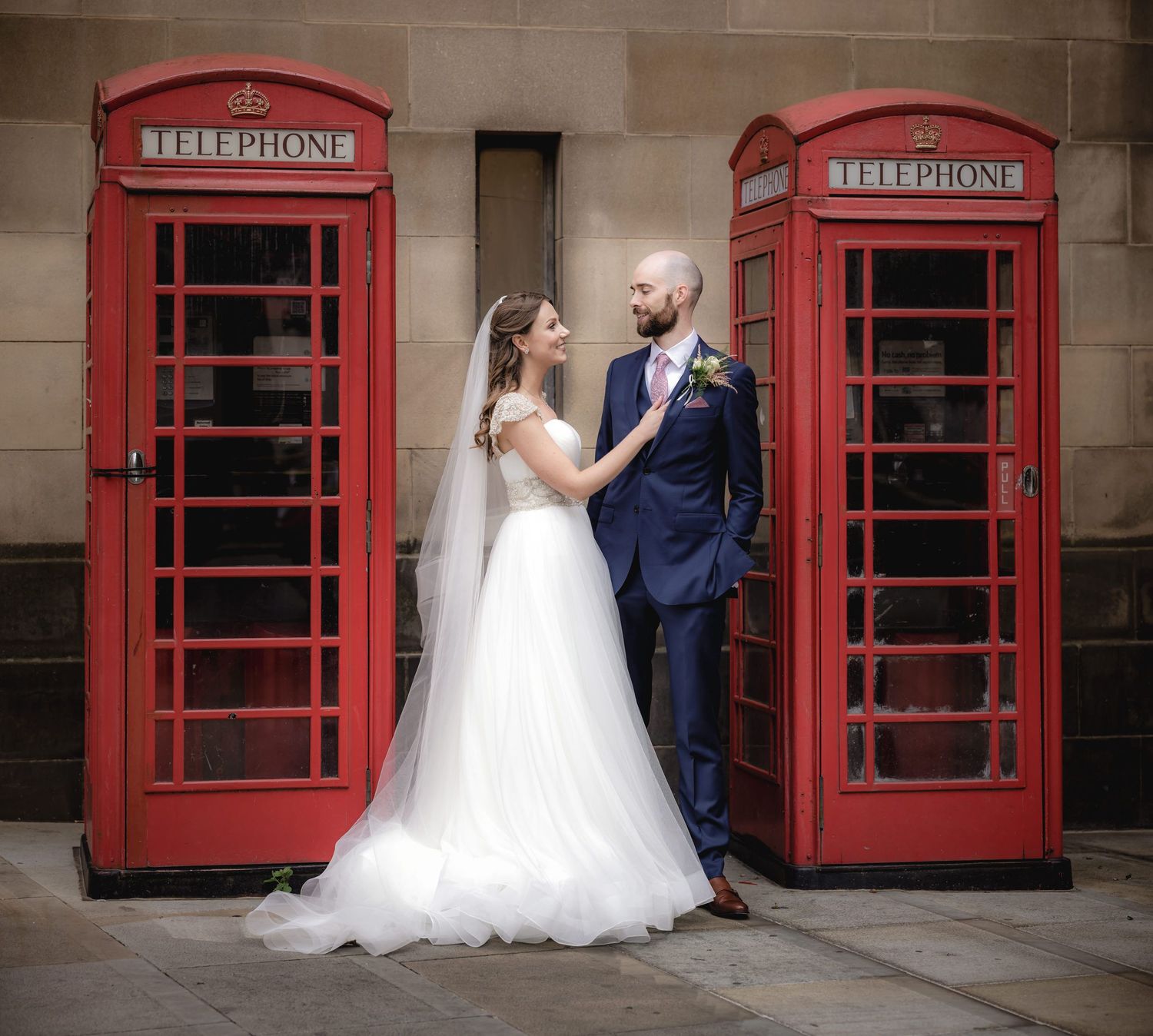 Bride and groom pose between two iconic red British telephone boxes on their wedding day.