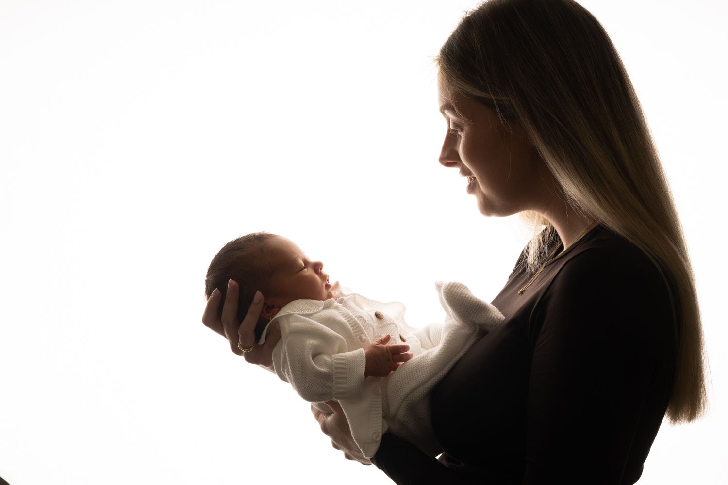 A mother tenderly holds her newborn baby in her arms, captured in a beautiful backlit silhouette portrait.