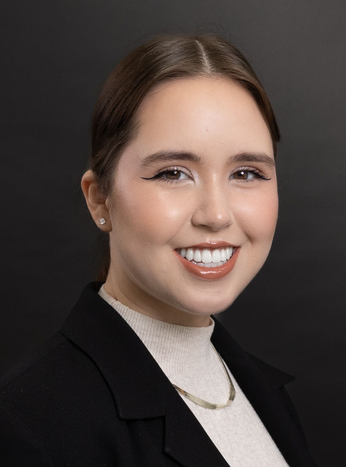 Professional headshot of a young woman with brown hair in a black blazer smiling against a dark background.