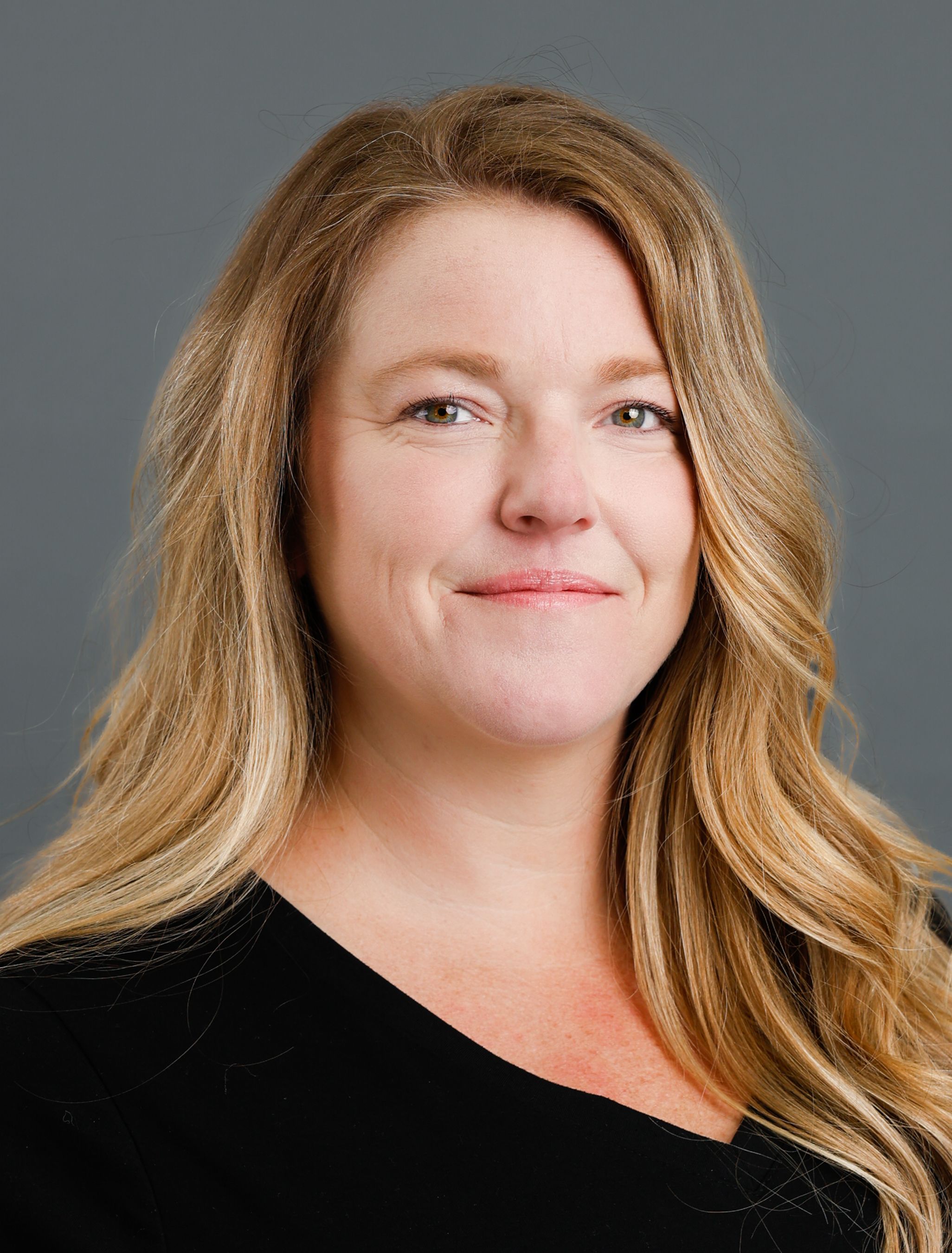 Professional headshot of a woman with long blonde hair wearing a black top against a gray background.