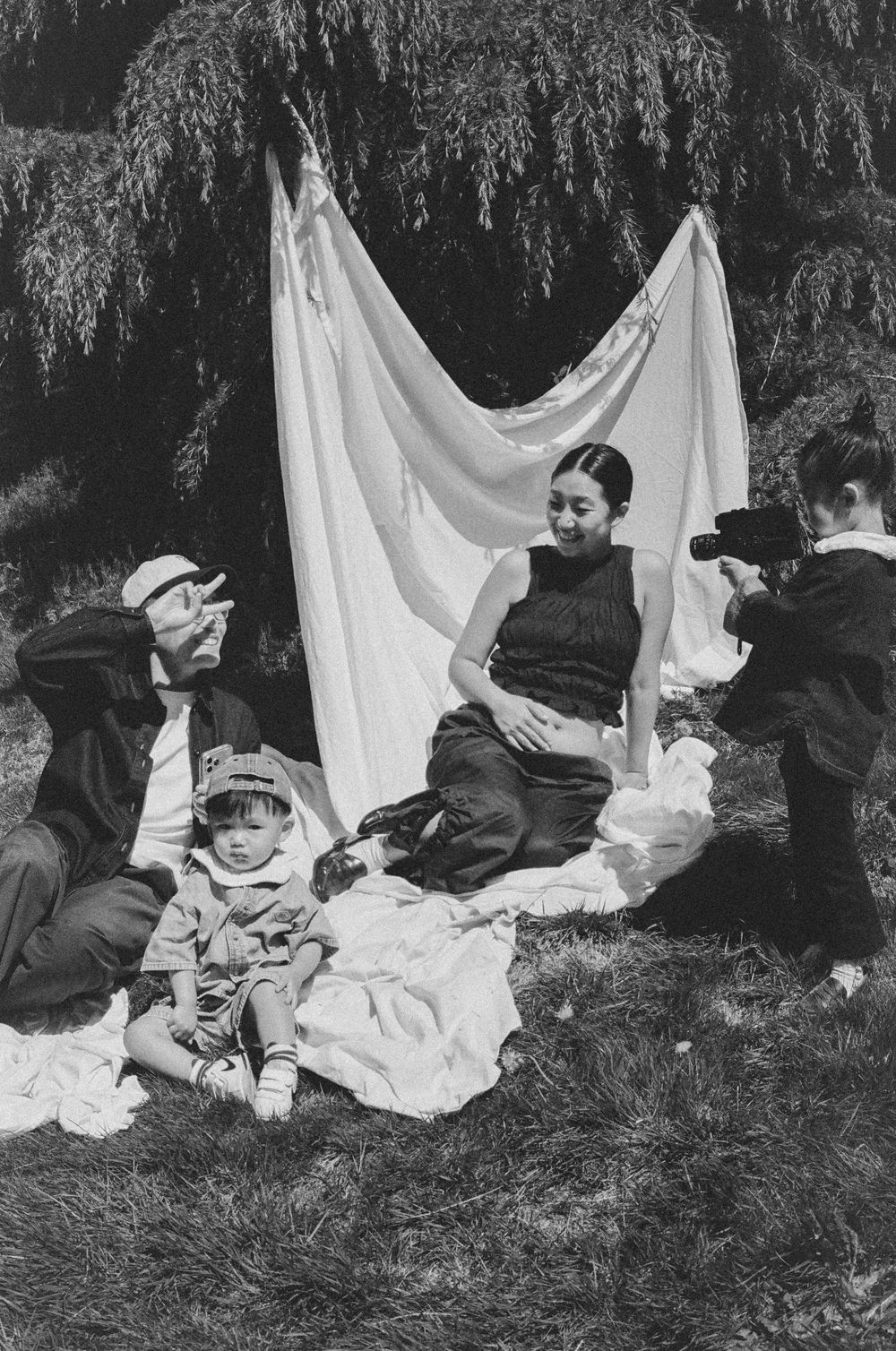 Black and white photo of a family posing outdoors with a white sheet backdrop while someone photographs them.