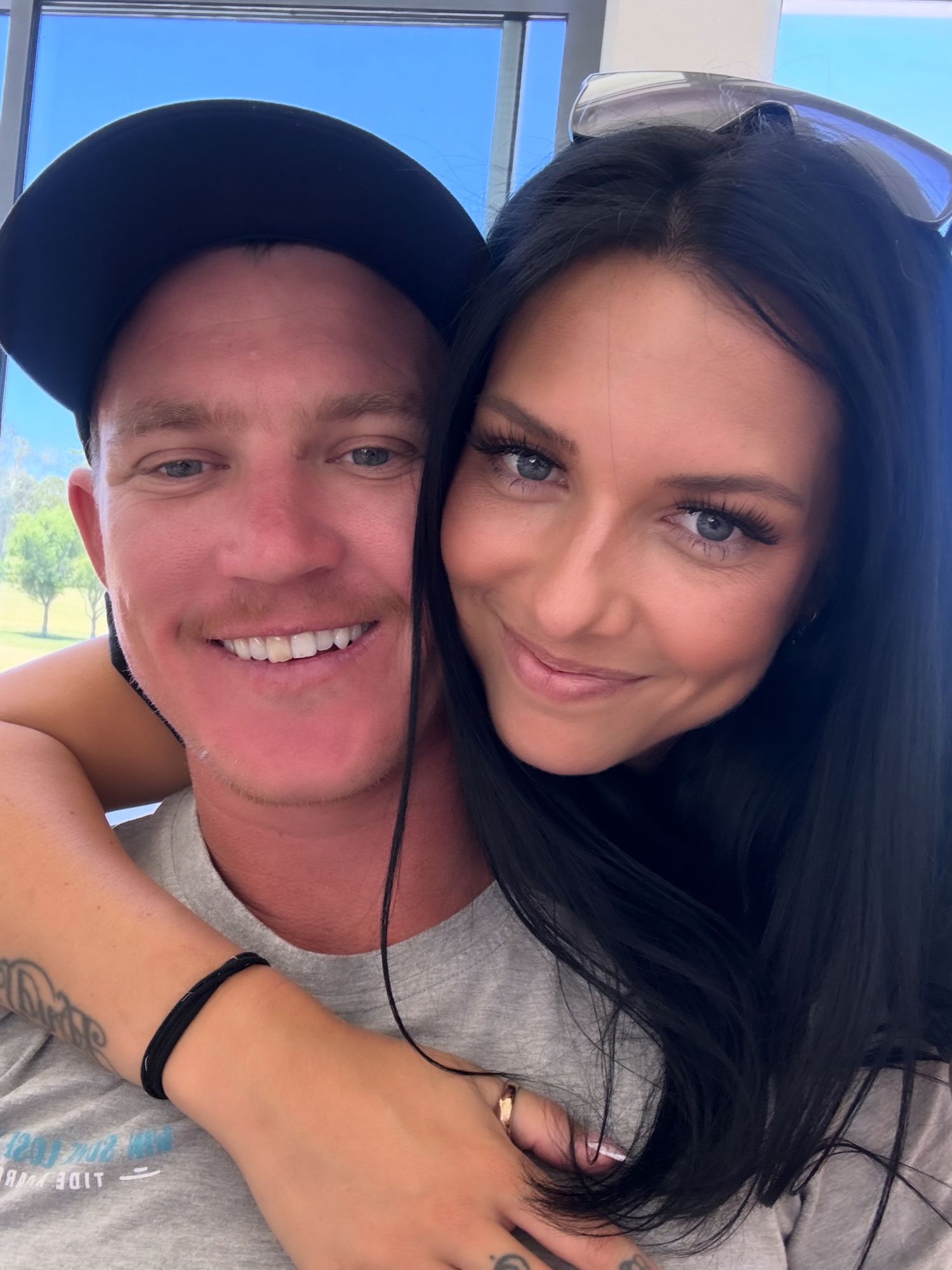 Smiling couple taking a close-up selfie together outdoors on a bright sunny day.